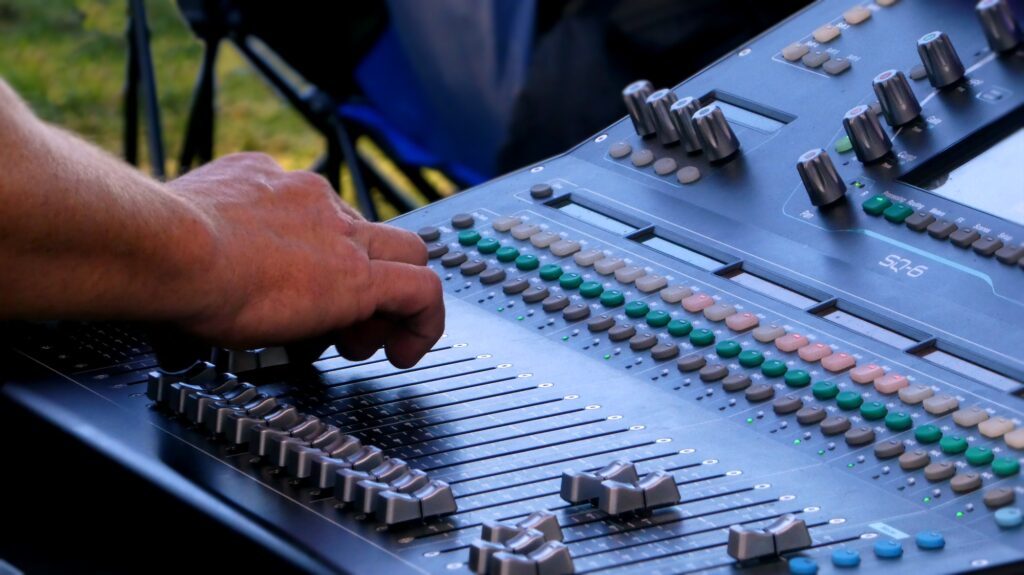 person pushing buttons on digital sound mixer at music festival
